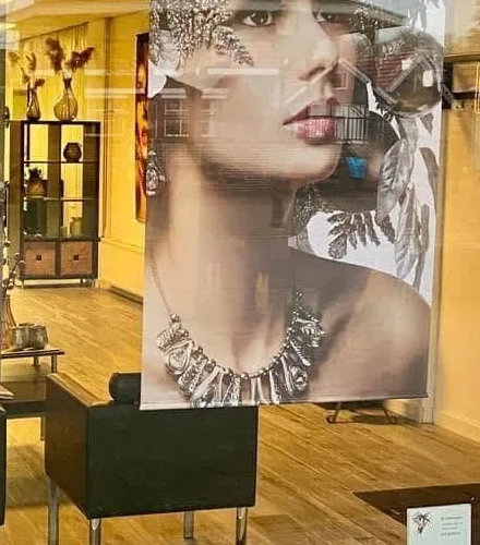 Door de etalage een kijkje in de salon, met stoelen en een kast met decoratie